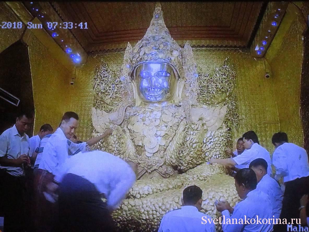 Посетители (мужчины) покрывают Будду золотыми листьями